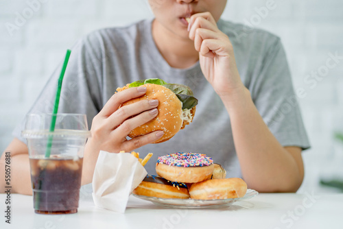 Woman eating fast food burger, fired chicken , donuts and desserts