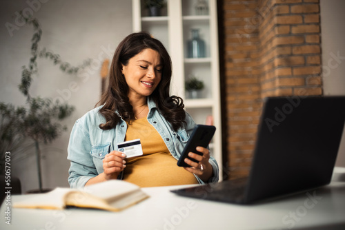 Pregnant woman shopping online at home. Happy woman with laptop and credit card... © JustLife