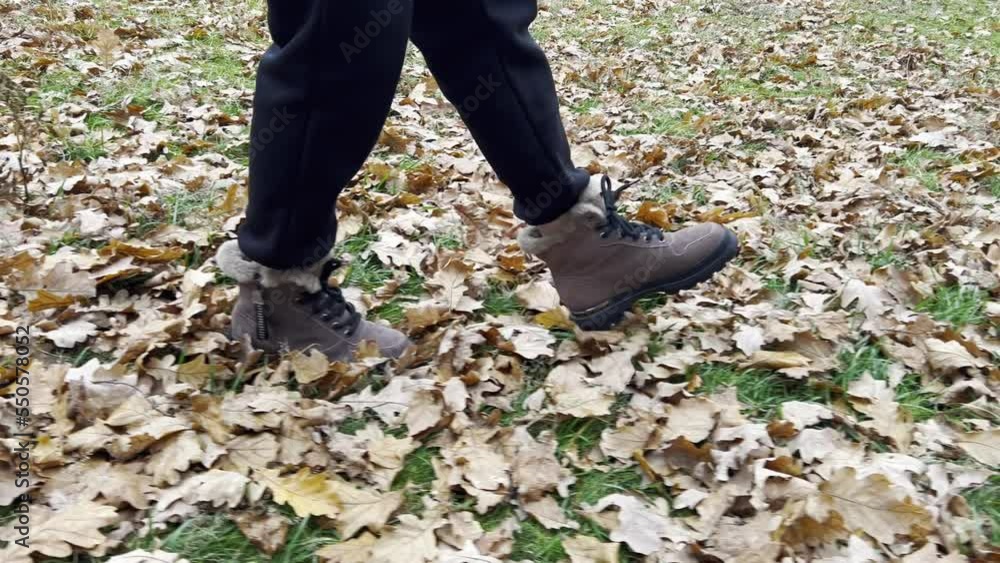 Women's feet, shod in winter boots, walk along the fallen leaves lying on the green grass. Women's feet, shod in winter boots, walk along the fallen leaves lying on the green grass.