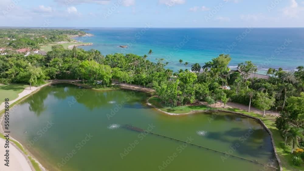 Aerial flight over private natural lake, tropical palm trees and blue Caribbean Sea in Background during sunny day - Punta Aguila in Dominican Republic Aerial flight over private natural lake, tropical palm trees and blue Caribbean Sea in Background during sunny day - Punta Aguila in Dominican Republic