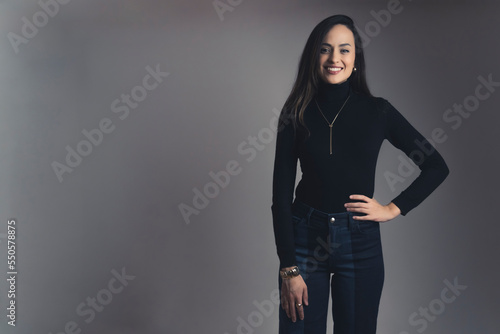 A medium shot of young brunette smiling woman standing with arm on hip. High quality photo