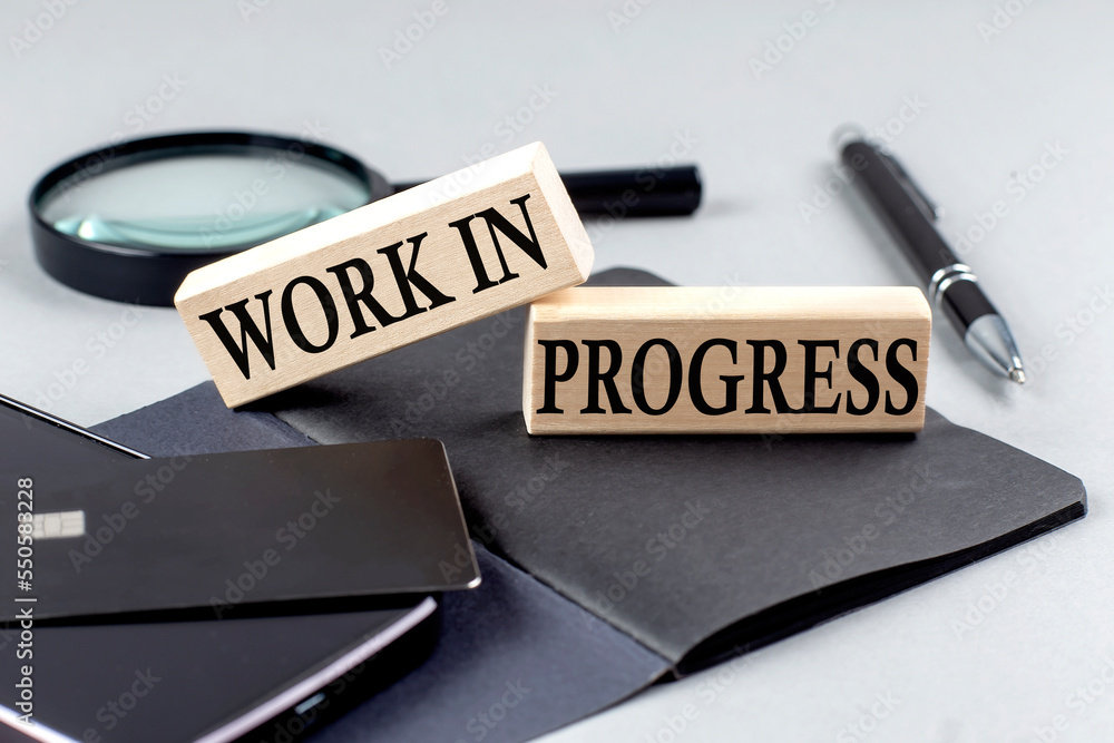 Fototapeta premium WORK IN PROGRESS text on wooden block on black notebook , business concept