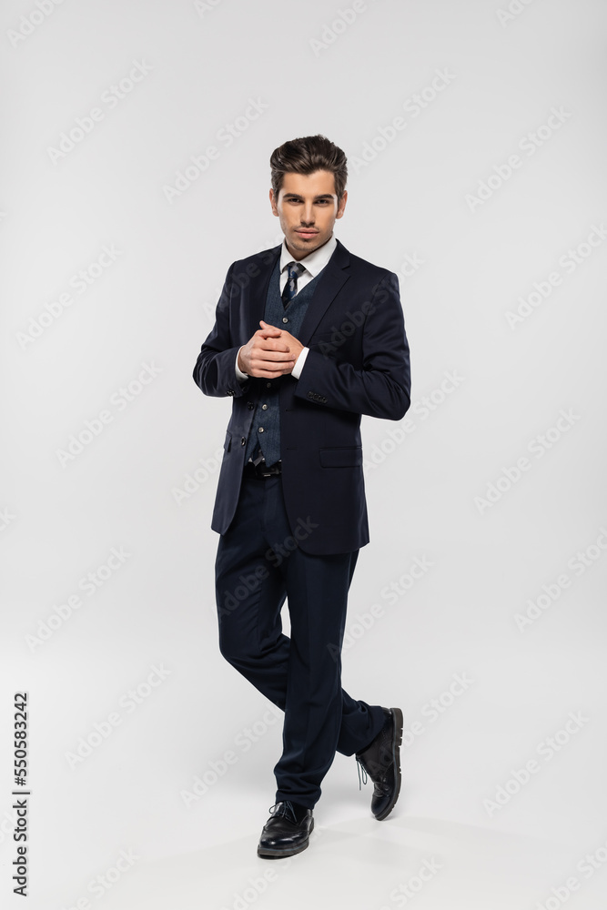full length of good looking businessman in suit standing and looking at camera on grey full length of good looking businessman in suit standing and looking at camera on grey