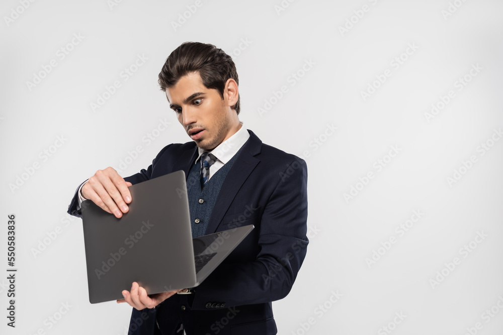 shocked businessman in suit looking at laptop isolated on grey shocked businessman in suit looking at laptop isolated on grey
