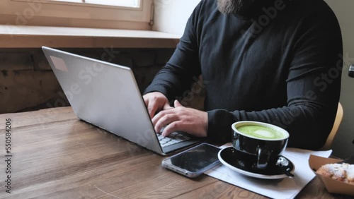 Male freelancer working with laptop computer, businessman work, typing on notebook while sitting at wooden table in modern coffee cafe with cup of coffee. Modern business, distance job, self employer.