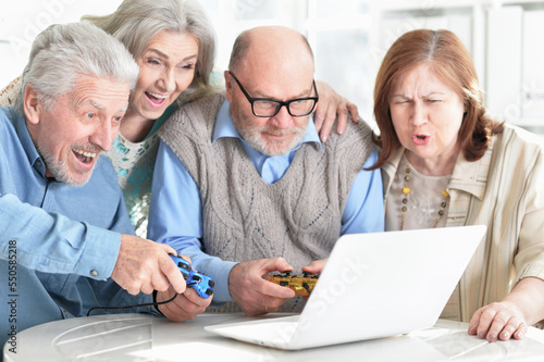 two senior couples sitting at table and playing computer