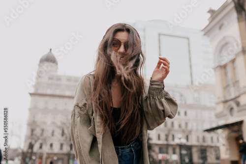 Outdoor photo of excited lovely girl with loose hair dancing, listening music and having fun in the city. 