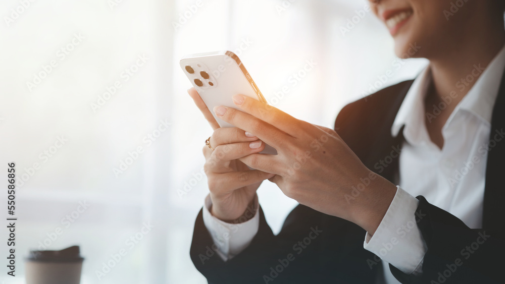 Beautiful Asian woman playing mobile phone in her break from work, she is a marketing manager of a startup company, female leader, supervisor, ceo. Female Leadership Concept.