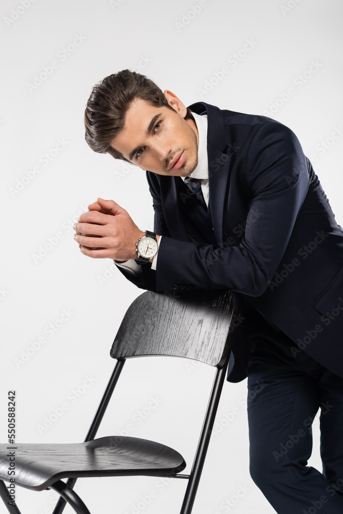 successful businessman in formal wear standing near chair isolated on grey successful businessman in formal wear standing near chair isolated on grey