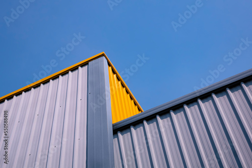 Bottom view of gray and yellow corrugated steel wall of modern warehouse building in different level against blue clear sky background