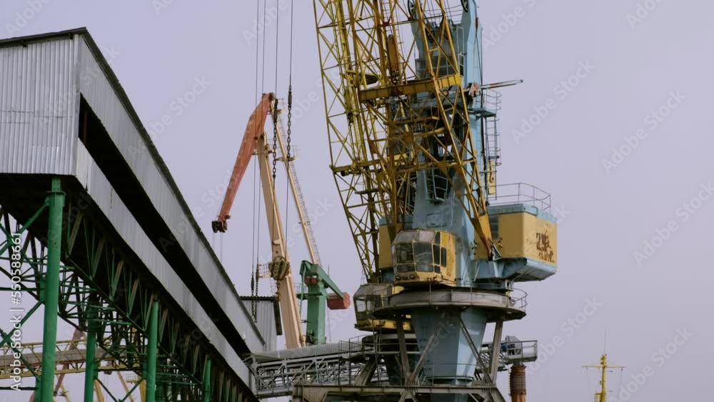 Operating process of huge high portal crane against grey sky. Truck and tower industrial machines carry heavy cargo from ships low angle shot Operating process of huge high portal crane against grey sky. Truck and tower industrial machines carry heavy cargo from ships low angle shot