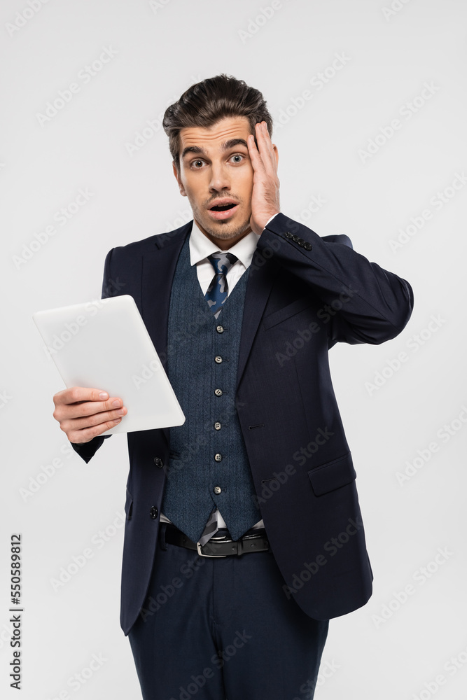 stressed young businessman in suit holding digital tablet isolated on grey stressed young businessman in suit holding digital tablet isolated on grey