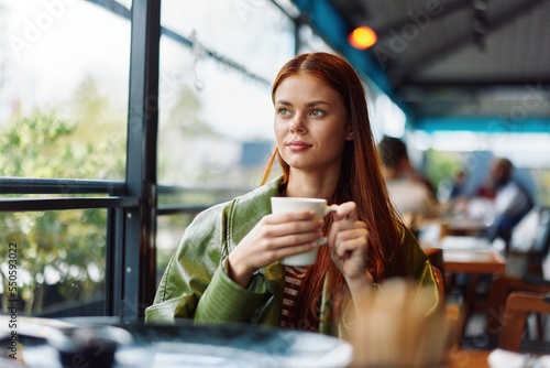 Stylish Influencer woman drinking a drink from a mug in a cafe and smiling looking out the window, content blogger © SHOTPRIME STUDIO