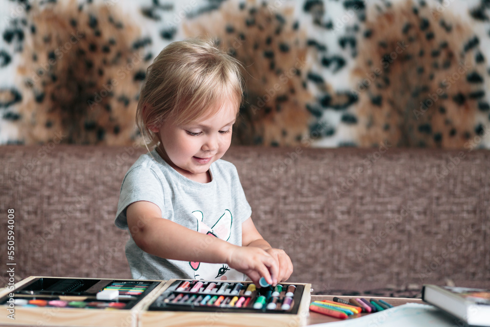 Fototapeta premium A little girl of 4 years old draws at the table at home with star-colored felt-tip pens.
