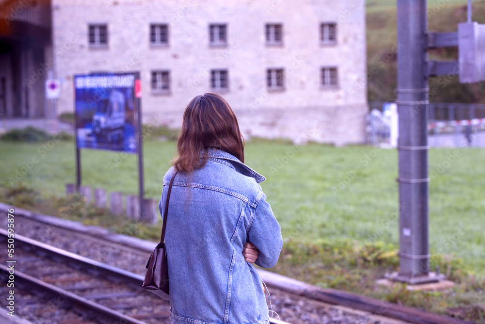 Young woman waiting at railway station of Matthorn Gotthard Railway at mountain village Hospental, Canton Uri, on a sunny late summer morning. Photo taken September 12th, 2022, Hospental, Switzerland.
