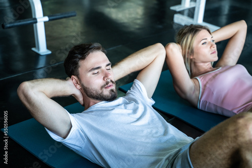Man and woman sit up on mat in sport gym working out