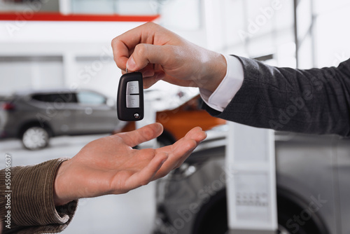 A sales manager in a suit passes the car key to the buyer against the background of the purchased car