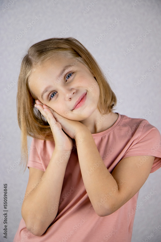 Portrait of a cute girl on a light background, a little blonde looks at the camera and smiles. The concept of joy, happiness and good mood. Portrait of a cute girl on a light background, a little blonde looks at the camera and smiles. The concept of joy, happiness and good mood.