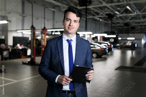 The manager for the reception of cars for repair with a tablet against the background of the service area of the dealership