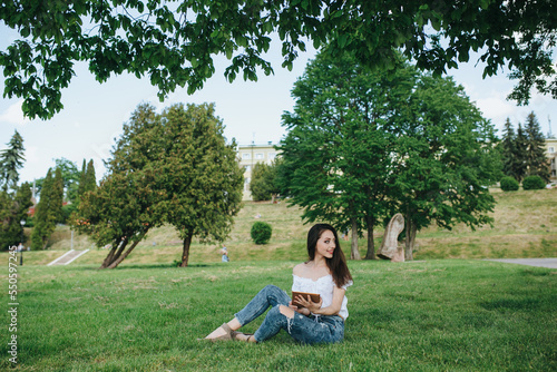 Young brunette woman, girl working with laptop, tablet and phone in green field, park with sunshine © andriyyavor