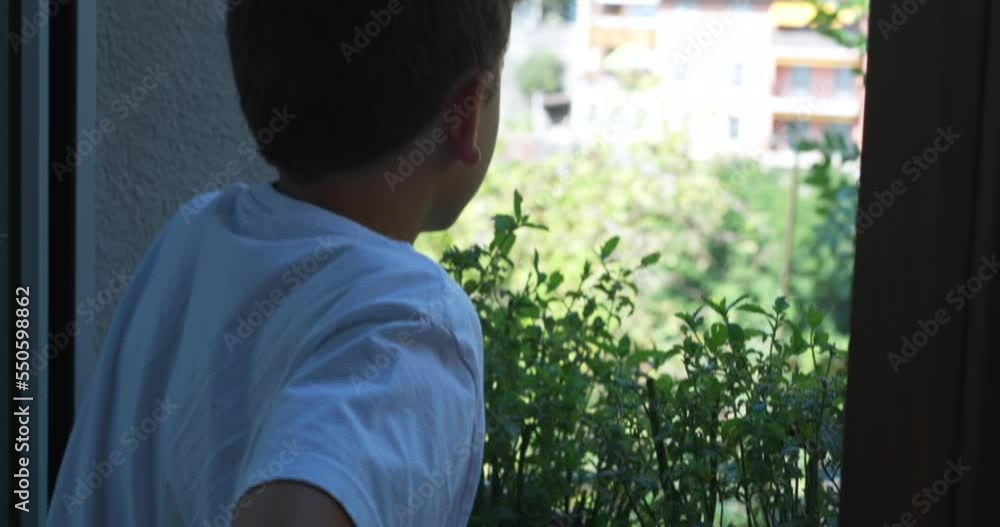 One young boy standing by window looking outside. Candid teen kid staring through home window observing beautiful sunny day One young boy standing by window looking outside. Candid teen kid staring through home window observing beautiful sunny day