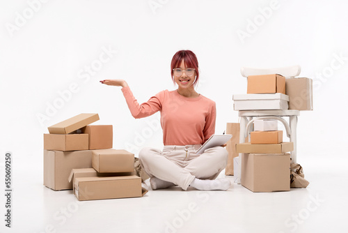 Beautiful  Asian girl in glasses is sitting on the floor. Packaging boxes are standing nearby. Moving to a new house, packing. Isolated on white background. Ad, moving and delivery concept