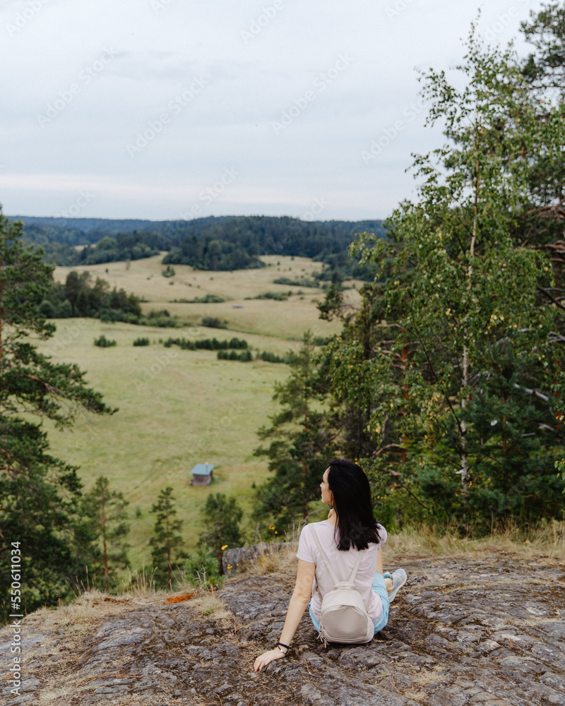 Girl tourist sits on a mountain overlooking a green meadow and pines