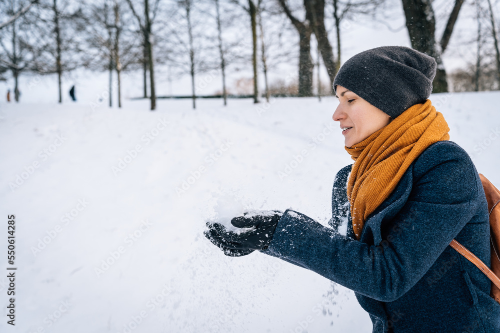 A woman in warm clothes throws snow with her hands