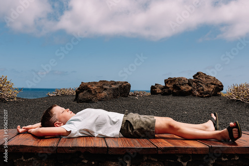 Serene kid lying on bench near sea photo