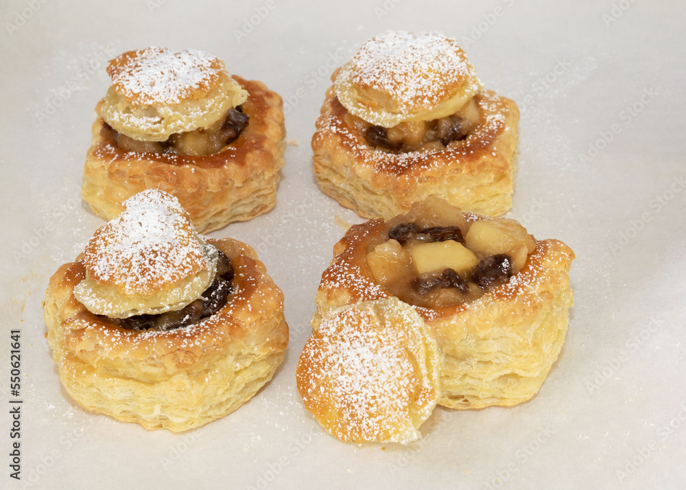 Apple and raisin stuffed puff pastry shells with sprinkled powdered sugar freshly baked on parchment paper.
