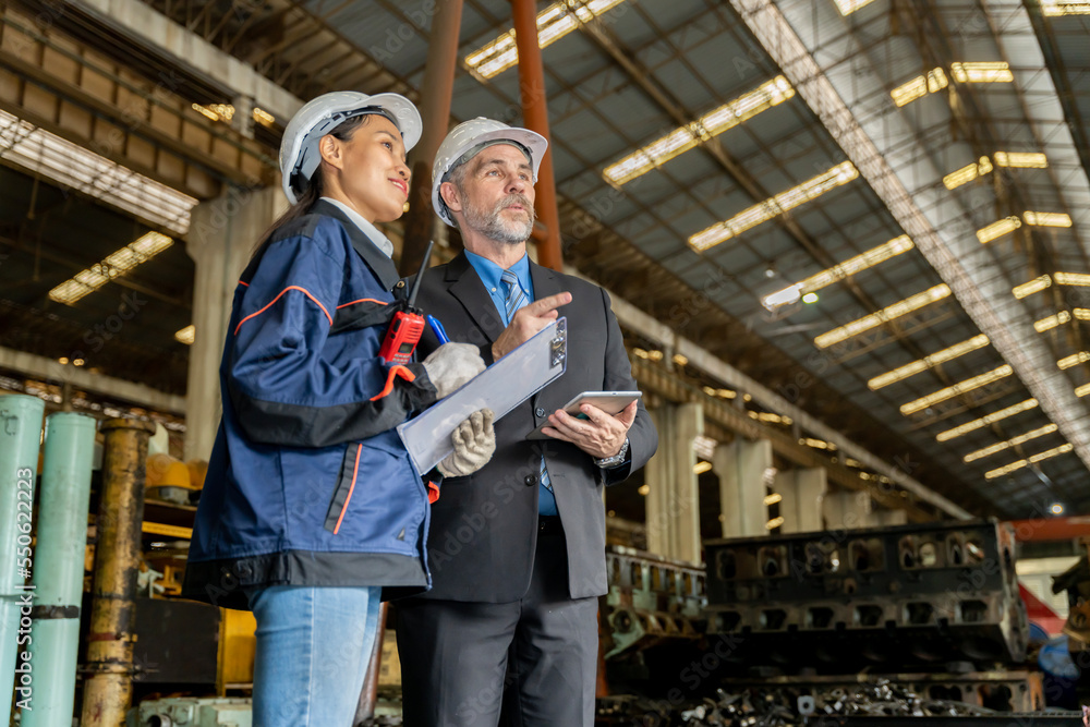 A business man inspects the work of an on-site worker at an old factory for rehearsing train engines. A business man inspects the work of an on-site worker at an old factory for rehearsing train engines.