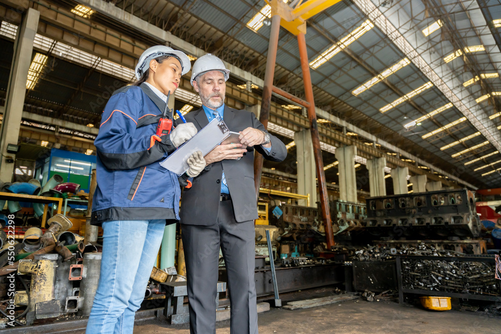A business man inspects the work of an on-site worker at an old factory for rehearsing train engines. A business man inspects the work of an on-site worker at an old factory for rehearsing train engines.