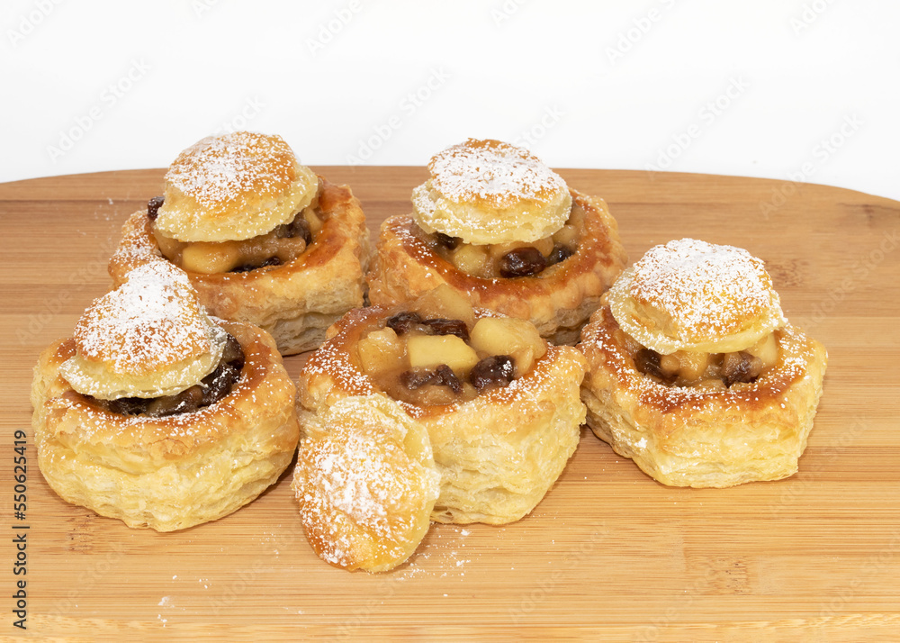 Apple and raisin stuffed puff pastry shells freshly baked are displayed on a wood board against a white background.