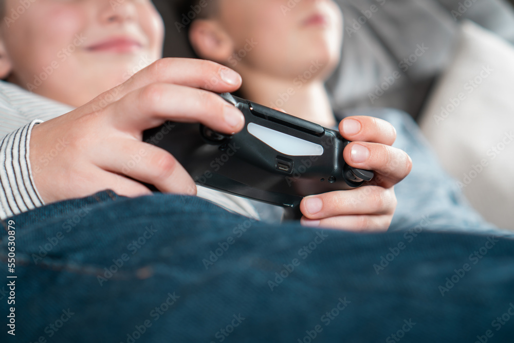 Hands of boy hold modified plastic joystick closeup, selective focus. Children lying on sofa play videogames. Hands of boy hold modified plastic joystick closeup, selective focus. Children lying on sofa play videogames.