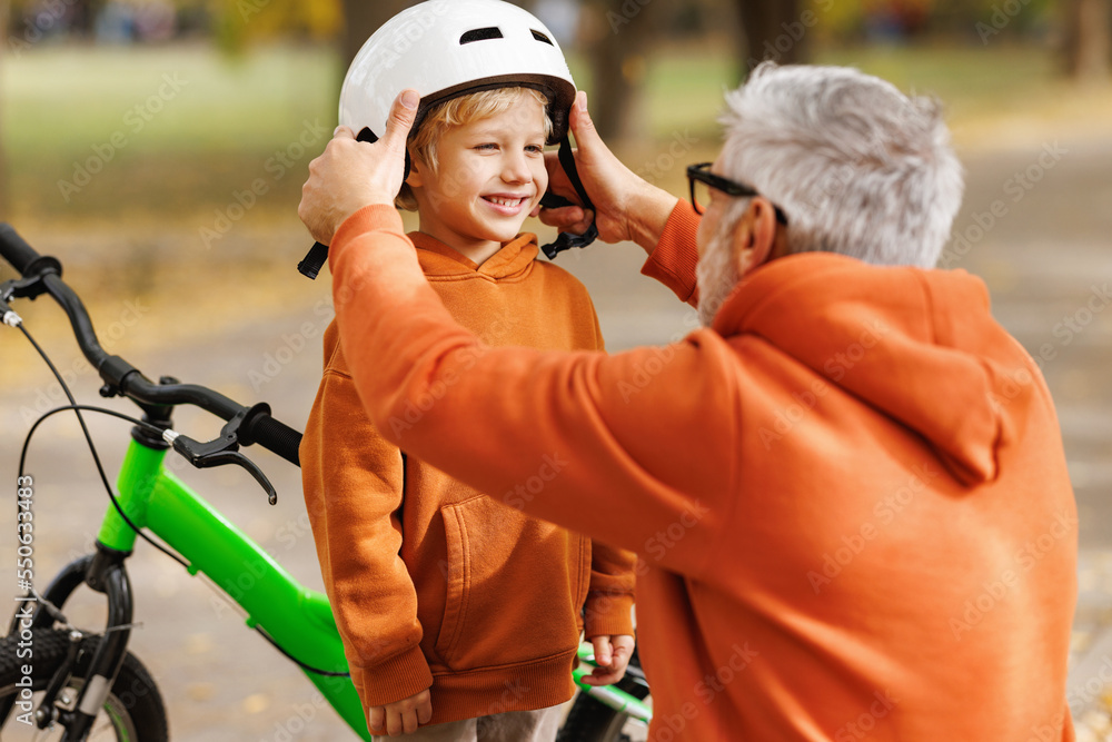 Happy family grandfather puts on grandson helmet for safe cycling in park Happy family grandfather puts on grandson helmet for safe cycling in park