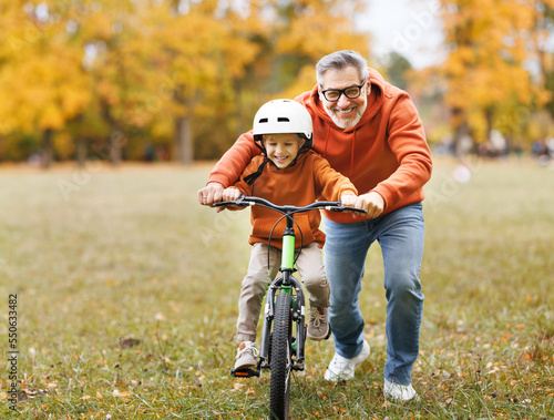 Fotografija Happy family grandfather teaches child grandson  to ride a bike in park