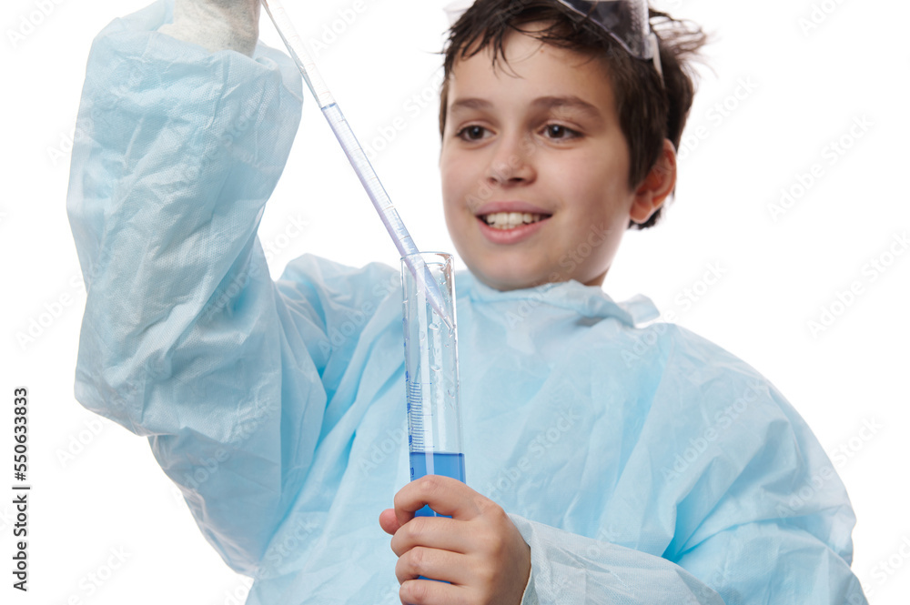 Close-up portrait of a smart school kid, teenage boy, a young chemist scientist, filling graduated pipette with blue chemical substance from a measuring lab cylinder, isolated over white background Close-up portrait of a smart school kid, teenage boy, a young chemist scientist, filling graduated pipette with blue chemical substance from a measuring lab cylinder, isolated over white background