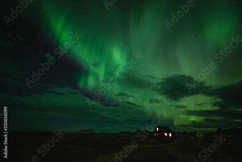 Cozy cottage in winter landscape by night with green aurora borealis