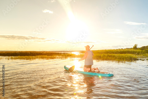 a man in shorts sits on a sup board at sunset in the water.