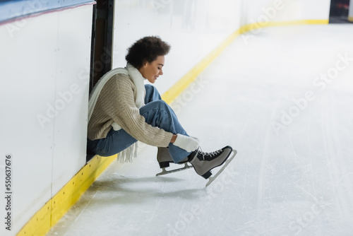 Fotografie Side view of smiling african american woman wearing ice skates on rink