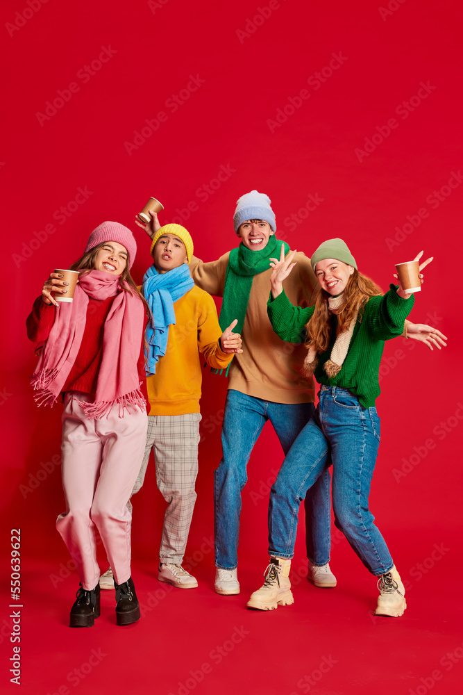 Group of young people, friends in winter clothes having fun together, posing isolated over red background