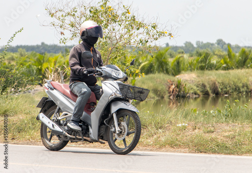 A man with helmet rides a motorcycle on a rural road