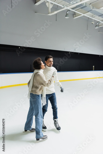 Young african american woman ice skating while spending time with boyfriend on rink