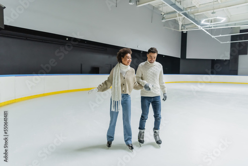 Young interracial couple holding hands while ice skating on rink