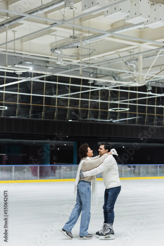 Side view of cheerful african american woman embracing boyfriend on ice rink