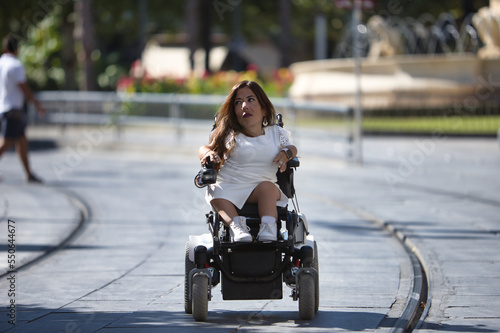 Disabled woman with reduced mobility and small stature in an electric wheelchair walking through the city center. Concept handicap, disability, incapacity, special needs, architectural barriers.