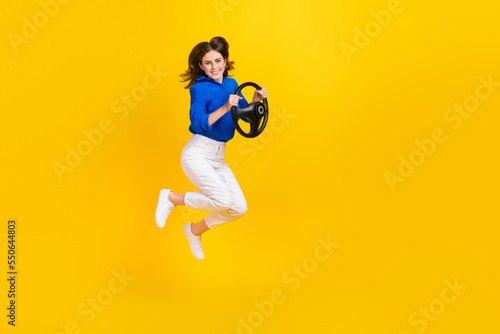 Full length photo of excited sweet girl dressed blue shirt jumping high car driver empty space isolated yellow color background