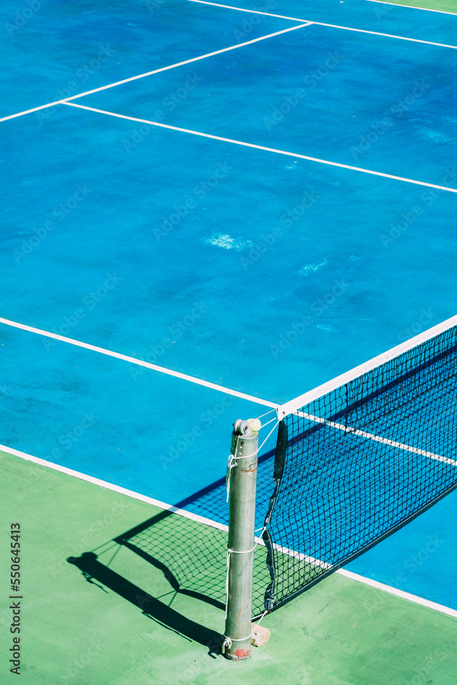 Deserted tennis court with greentrees in background in a public park on a sunny summer morning Deserted tennis court with greentrees in background in a public park on a sunny summer morning