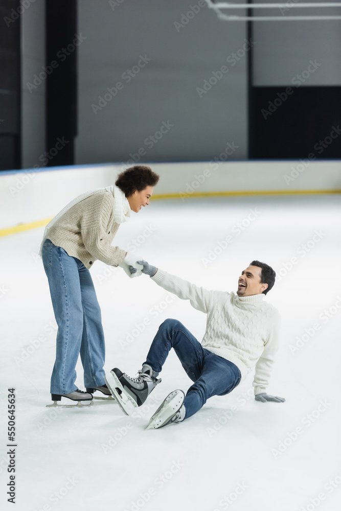 Cheerful african american woman holding hand of boyfriend on ice rink