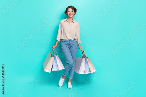 Full length photo of positive pretty lady wear trendy outfit two hand hold carry bags rejoice low price isolated on cyan color background